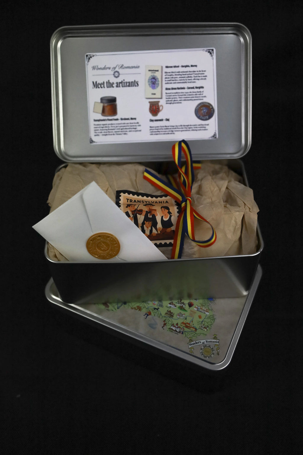 Metal tin with various items including a certificate, a bag, and a small plant on a black background