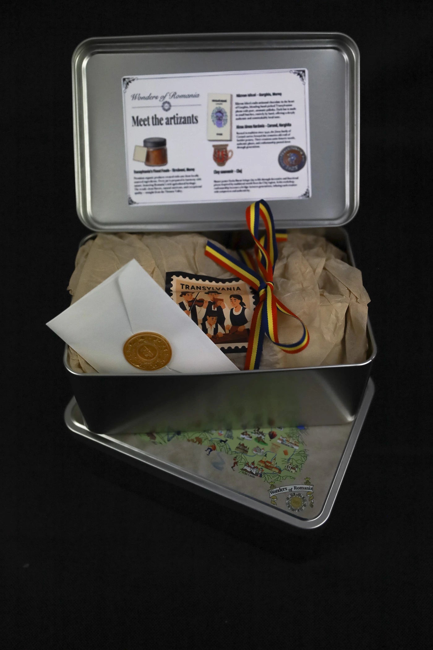Metal tin with various items including a certificate, a bag, and a small plant on a black background
