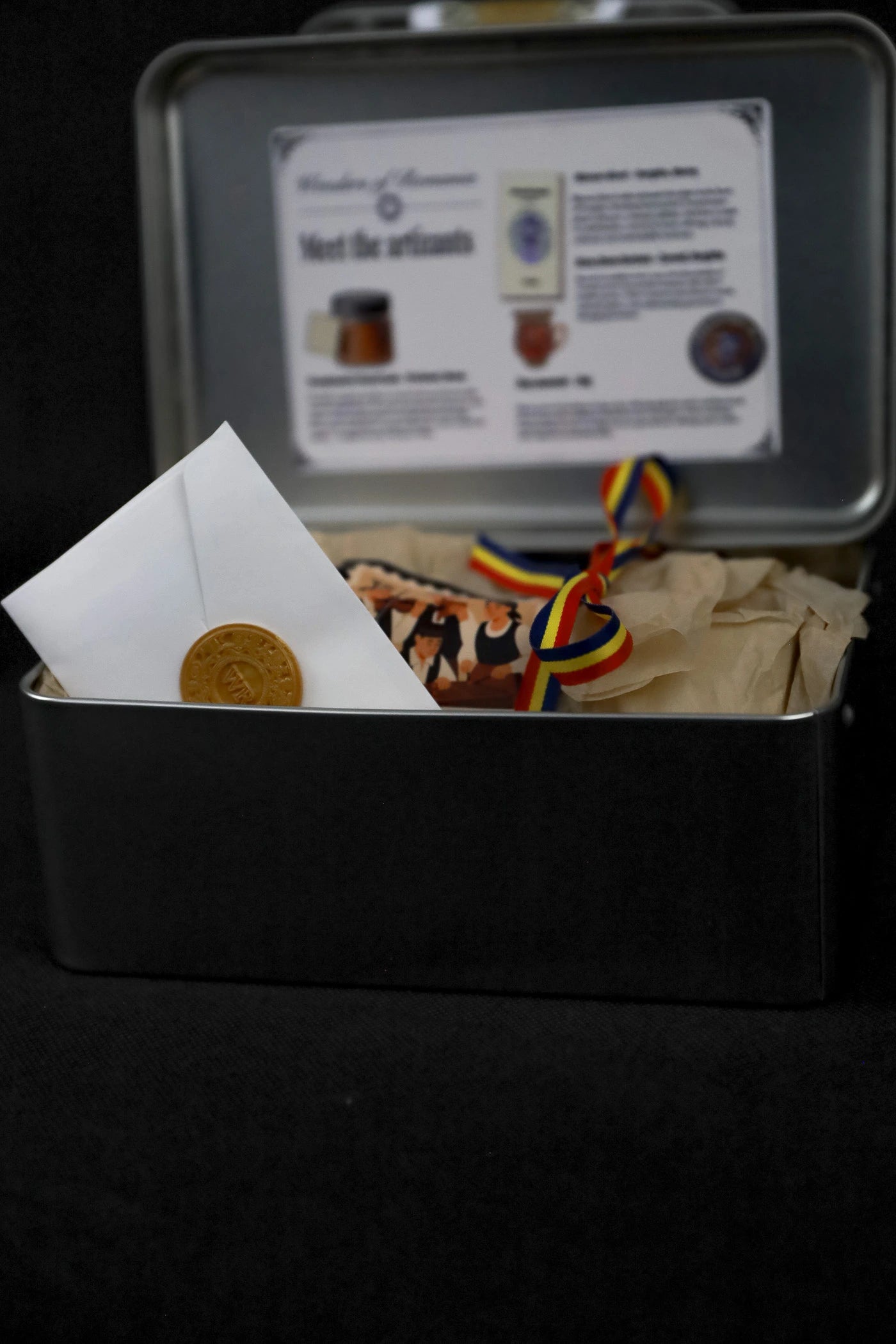 Open black tin box with contents and a label on a dark background